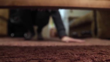 Yatağın altında bir şey arayan bir adam. El bir nesneyi yokluyor.