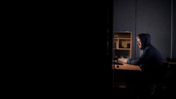 一个戴着头巾的留着胡子的男人在台灯旁边的电脑上工作 男职员晚上在一间黑暗的房间里工作 在线处理文档 黑客或程序员 — 图库视频影像