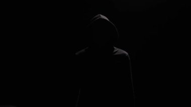 Siyah kapüşonlu, karanlık arka planda duran kimliği belirsiz bir adam kameraya doğru işaret veriyor. Hacker, suçlu ya da anonim, iyi niyet gösteriyor.