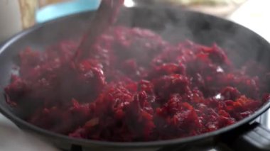 Parçalanmış pancar kökünün pişirildiği kızartma tavasının yakın çekimi. Bir ev hanımı, mutfaktaki bir gaz sobasında mutfak spatulasıyla dilimlenmiş pancar kökü karıştırıyor..