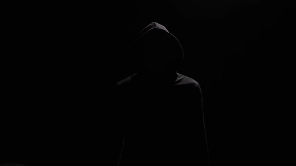 黒いフーディーの身元不明の男は 暗い背景に立って カメラに親指を示しています ハッカー 犯罪者または匿名は 親指がジェスチャーを示しています — ストック動画