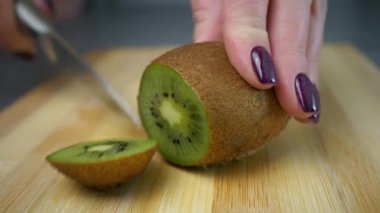 Kızın biri olgun bir kiviyi tahta bir kesme tahtasındaki bıçakla dilimlere ayırıyor. Yakın plan. Olgun meyve kesimi. Vitamin alımı. meyve diyeti. Sağlıklı yemek..