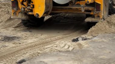 Bir inşaat şantiyesinde tamir sırasında traktör kazısı ters yönde gidiyor. Şehirdeki iletişimin tamiri. Yükleyici geri gidiyor. Sürücü bir traktörün büyük tekerleklerine yakın çekim.