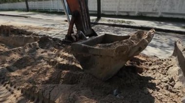 Büyük kazılmış bir siperin arka planına karşı büyük bir kazıcı kovası. Yol onarımı sırasında traktör buldozerinin etrafında dönen vibratörlü kamera..
