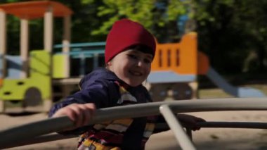 Güneşli bir günde oyun alanında atlıkarıncaya binerken şapkalı şirin bir kız gülüyor ve gülümsüyor. Çocuk hayatın tadını çıkarıyor ve eğleniyor..
