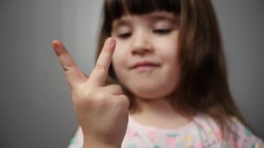 Gri arka planda, sağ elinde beşe kadar sayan küçük bir kızın izole edilmiş portresi. Sevimli bir çocuk gülümsüyor ve 1 'den 5 parmağa kadar sayıyor..