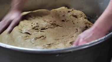 Bir fırında, bir fırıncı büyük bir hamur karıştırıcısında ekmek hamuru yoğururken hamuru nazikçe yassılaştırır. Fırın ürünlerinin üretimi.