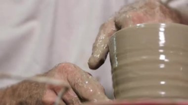 Çömlekçinin tekerinde kilden sürahi yapan bir çömlekçinin eline yakın çekim. Yaşlı bir adam kendi atölyesinde geleneksel metodu kullanarak el işi çömlek yapıyor..