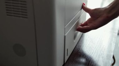 Kız ofis çalışanı ya da sekreter yazıcıdaki kağıt tepsisini açar ve yeni bir kağıt koyar. Bir kadın belge basmak için bir yazıcı hazırlıyor.