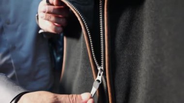 Kamera bir adamın elini takip ederken, fermuarın fermuarı bir yeleğin fermuarını açar. Moda endüstrisi, tekstil ve giysi konsepti. Parmakları olan fermuar. Tekstil endüstrisi.