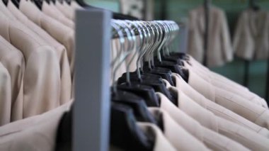 Birçok yeni bej ceket mağazadaki bir askıda asılı. Taze dikilmiş giysiler trempellere asılır. Dikiş fabrikası, tekstil fabrikası ya da giyim mağazası.
