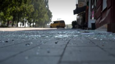 Kırık bir arabanın arka planında kaldırım taşlarından yapılmış yaya kaldırımındaki cam kırıklarının yakın çekimi. Bir patlama, kaza ya da felaketin sonucu..