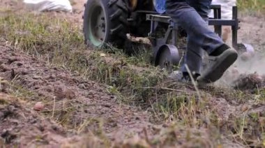 Patates kazıcısının yakın çekimi traktörün arkasında. Özel çiftlikte patates topluyorum. İnsanlar traktörle patates kazıyor. Çiftçi sebze bahçesinde kök sebze toplarken traktör sürüyor..