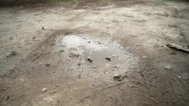 Sonbahar botları içinde bir adamın ayağının bastığı kirli bir su birikintisine yakın çekim. Kırsal bir yolda çamur birikintisi.