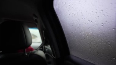 Araba sürerken arabanın camına yağmur damlaları düşer. Yağmurlu havada seyahat ederken bir araba, otobüs veya toplu taşıma aracındaki birinci şahıs görüntüsü. Yolcu koltuğundaki POV. Yağmur damlalarına odaklan.
