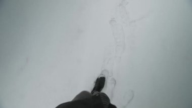 POV kışın karda yürür, erkek botları taze karda ayak izleri bırakır. Kış mevsiminde dağlarda ya da ormanlarda yürüyüş ya da yürüyüş. Kışın yürüyen siyah çizmeli bir adamın bacakları. ilk kişi görünümü