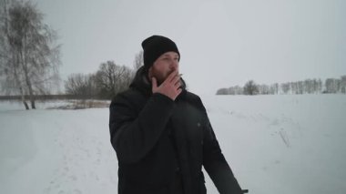 Kızıl sakallı bir adam tarlada yürüyor ve sigara içiyor. Uzağa dikkatlice bakıyor. Sakallı, kışlık ceketli ve şapkalı bir adam kışın karlı arazide yürür ve kar altında sigara içer.