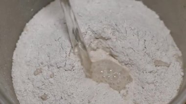 Erkek müteahhit, alçı taşı bazlı kuru bir karışım ve yakın çekim görüntüsüyle kovaya su döker. Duvarları çürütmek ve yıkmak için havan topu hazırlığı. Onarım Çalışması.