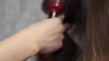 Anne kızının saçını bir saç kurutma makinesiyle kurutur ve bir tarak ile tarar. Anne kızına bakıyor..