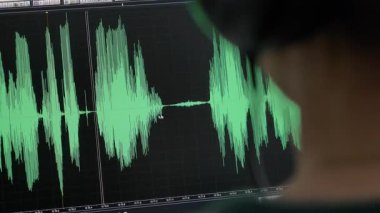 Kafasında kulaklıkla stüdyoda müziği kontrol eden bir ses mühendisinin arka görüntüsü. Bir ses düzenleyici bir bilgisayarda bir ses parçasını düzenler.