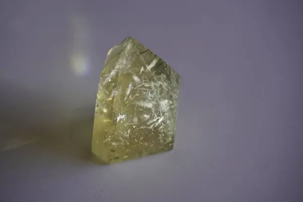 Beyaz arkaplanda yansıması olan altın rengi kuvars kristali.