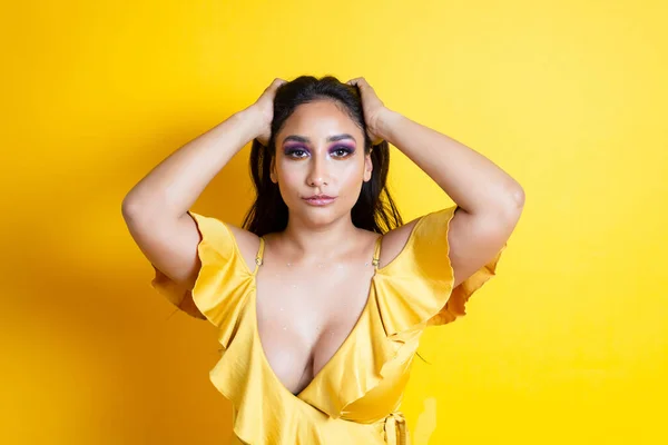 portrait of elegant and sensual hispanic young woman holding her hair in yellow dress