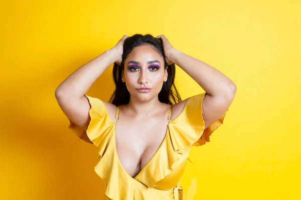 優美で官能的なヒスパニック系の若い女性の肖像画黄色のドレスで彼女の髪を保持 ストック画像