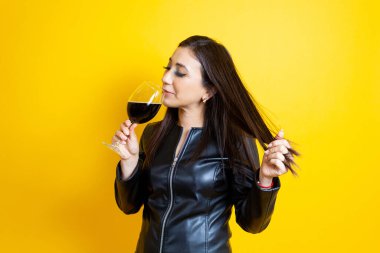relaxed latin caucasian woman drinking glass of red wine in front of isolated yellow background