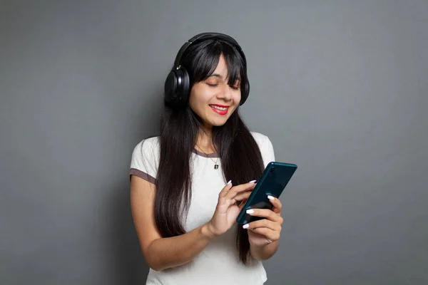 young mexican woman listening to music with headphones and using smart phone