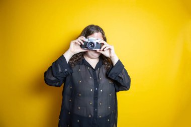 overweight woman using old camera on isolated yellow background