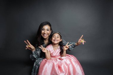 elegant latin mom and daughter sitting waving and looking at the camera