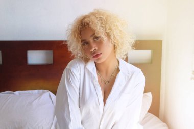 Güzel Afrikalı Meksikalı kız yatağa oturmuş kameraya bakıyor.