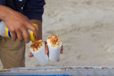 Meksikalı gıda tedarikçisi, mısır taneleriyle bardağın üzerine acı biber tozu döküyor. esquites