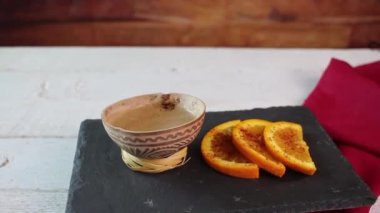 Geleneksel bardakta tekila ya da mezcal shot, kırmızı biberli portakal dilimlerinin yanında taş tabakta yavaşça dönüyor.