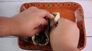 Yüksek açılı, tanınmayan biri Carnitas taco yerleştiriyor ve kil tabağa yeşil sos koyuyor. Meksika yemeği