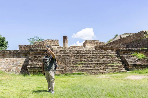 Traveler man making video call with his phone in front of the pyramid of Monte Alban Oaxaca