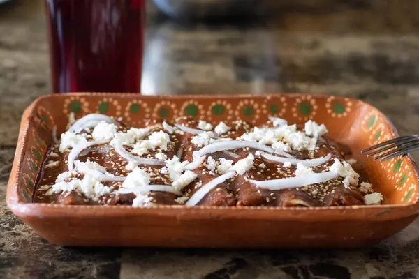 stock image Front view of plate with enchiladas with red mole sauce with onion and cheese. Mexican food