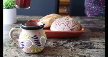 Geleneksel Meksika bardağına kahve döken kişinin gerçek zamanlı görüntüsü. Yanında ekmek ve Meksika yemeği.