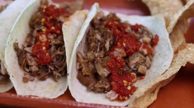 Kişi kırmızı sosu dökerken, Carnitas tacolarına soğan ve limon koyarken. Meksika yemeği