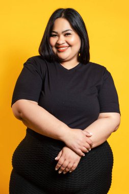 Siyah gömlekli, sarı arka planda sırıtan şişman bir kadın.