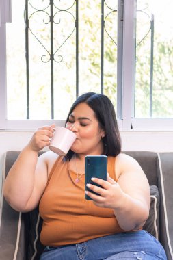 Ayrıca koltukta oturan, kahve içen ve akıllı telefonlara bakan Latin bir kadın.