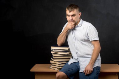 Avrupalı görünümlü bir adam düşünceli bir bakışla masada oturur. Yakınlarda bir yığın kitap var. Öğretmen derse hazırlanıyor.