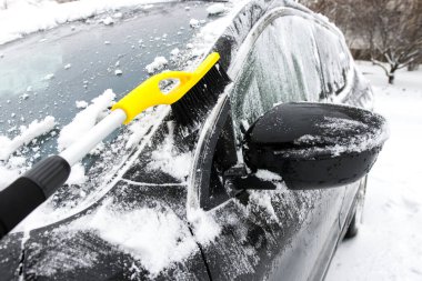 Güneşli bir günde bir adam kar yağdıktan sonra arabayı temizler. Kar fırtınasından sonra bir kış günü arabayı kardan temizlemek ve temizlemek..