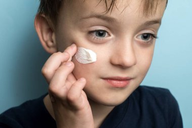 Avrupalı görünümlü küçük bir çocuk yüzüne krem sürüyor..