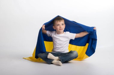 a little boy is sitting on the floor and holding the flag of Ukraine