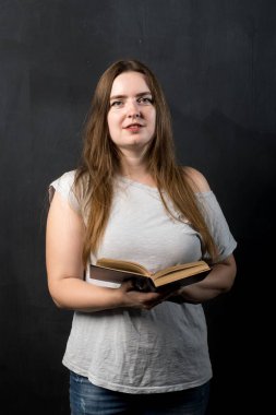 vertical portrait of a girl of European appearance on a black background with a book in her hands.