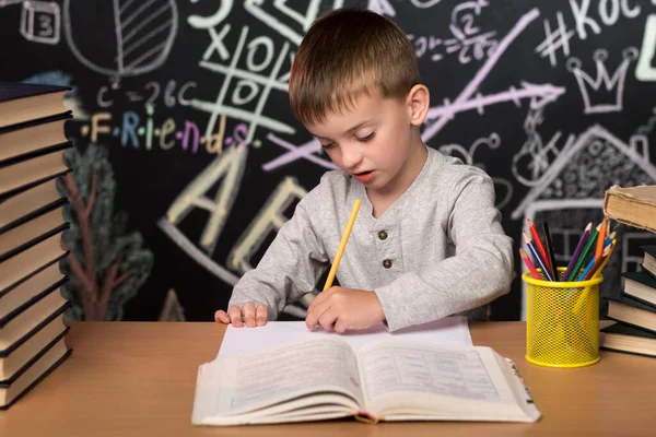 Ein Kleiner Junge Europäischen Aussehens Sitzt Einem Schreibtisch Und Schreibt — Stockfoto
