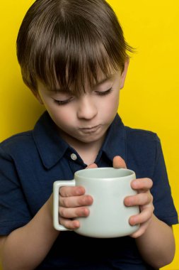 Avrupalı görünümlü bir çocuk elinde bir bardak süt ya da su tutuyor. Aşağı bak.