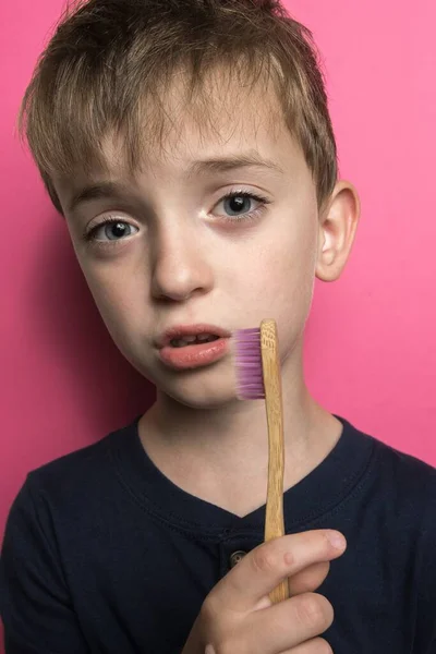 Chłopiec Europejskim Wyglądzie Trzyma Dłoniach Bambusową Szczoteczkę Zębów Różowym Tle — Zdjęcie stockowe