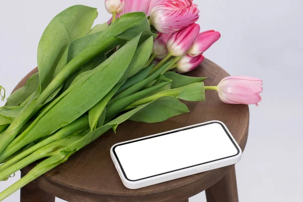 pink tulips on a chair next to a smartphone on a white background. place for text, mockup